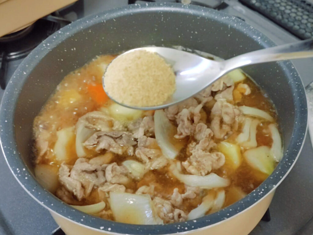 鍋で煮込んでいる肉じゃがに沖縄の恵み糖を入れるところ